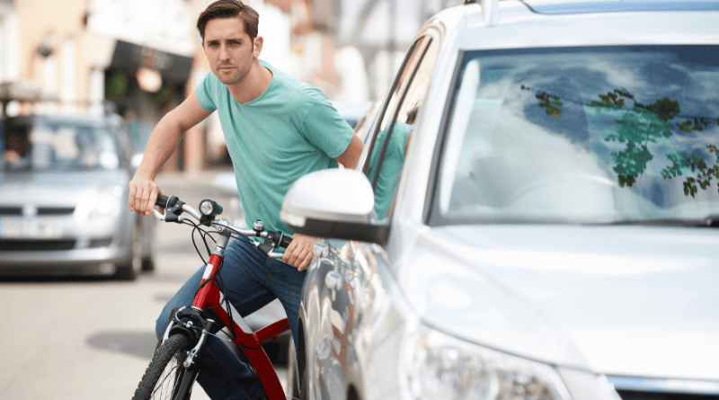 um ciclista saindo de trás de um carro